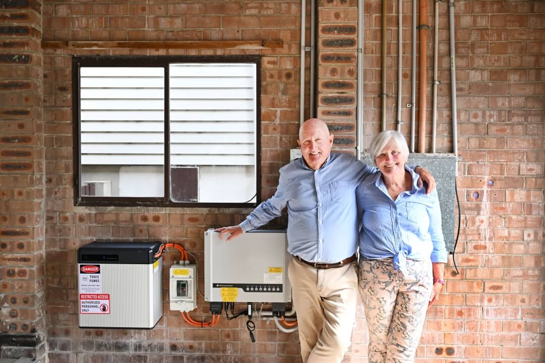 A senior couple standing in their garage next to a home battery and inverter